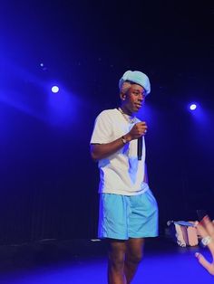 a man in blue shorts and a white t - shirt is standing on stage with a microphone