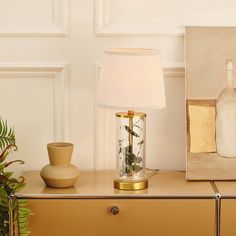 a table with a lamp, vase and painting on it next to a potted plant