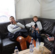 two people sitting on a black leather couch with water bottles and drinks in front of them