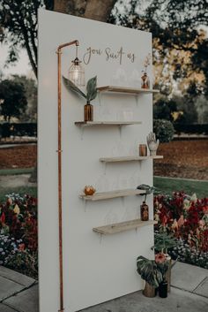 a white refrigerator sitting on top of a sidewalk next to a flower garden and trees