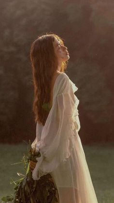 a woman in a white dress is holding a bouquet and looking off into the distance