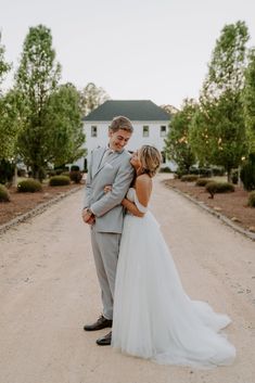 a bride and groom standing in the middle of a dirt road with their arms around each other