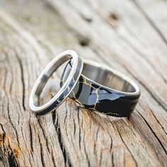 two wedding rings sitting on top of a piece of wood with black and white marble