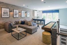 a living room filled with furniture and a pool table in front of a brick wall