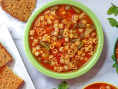 a bowl of pasta soup next to two slices of bread on a white counter top