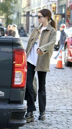 a woman standing next to a car on a brick road with her hand in her pocket