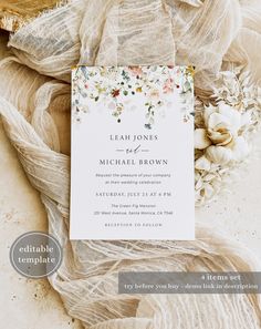 a wedding card with flowers on it sitting next to some sheer fabric and a flower bouquet