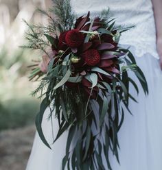 a bride holding a bouquet of red flowers and greenery