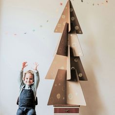 a little boy standing next to a cardboard christmas tree