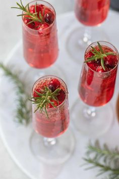 three glasses filled with red liquid and garnished with greenery on the rim