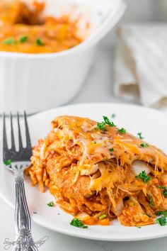 a white plate topped with lasagna covered in cheese and parsley next to a fork