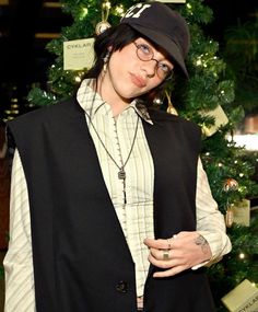 a woman wearing glasses and a hat standing in front of a christmas tree with her hands on her hips