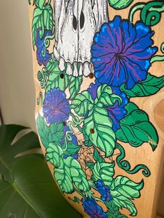 a wooden chair decorated with flowers and a skull on the front side, sitting next to a green leafy plant