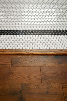 a white and black tiled floor in a bathroom next to a wood flooring area