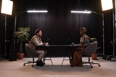 two people sitting at a table with microphones in front of them and lights behind them