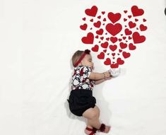 a baby is laying on the floor with hearts drawn on it's wall behind her