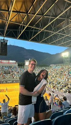 a man and woman standing next to each other in front of a stadium full of people