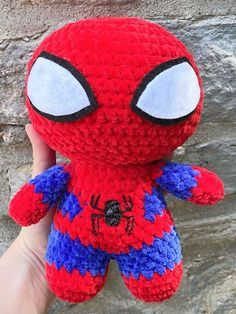 a hand holding a red and blue spiderman stuffed animal in front of a stone wall