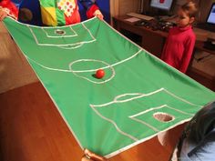 a child holding up a green table with white lines on it and balls in the air