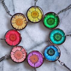 six different colored flower necklaces sitting on a marble surface with silver chain and pendant