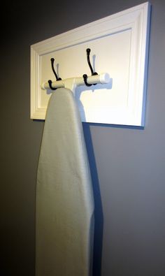 an ironing board is hanging on the wall next to a towel rack with two hooks