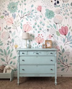 a blue dresser sitting next to a wall with flowers on it