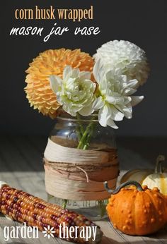 there is a vase with flowers and corn on the cob next to pumpkins