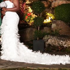 a woman in a white dress standing next to a stone wall with flowers on it