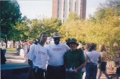 two men standing next to each other in front of trees and people on the sidewalk