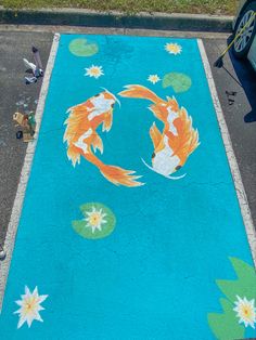 two fish are swimming in the water on a blue surface with flowers and leaves painted on it