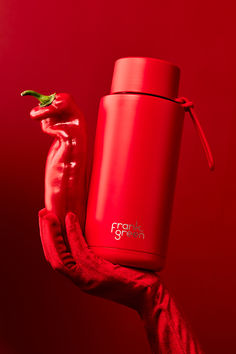 a person's hand holding a red thermos and a hot pepper on a red background