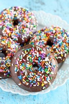 three chocolate donuts with sprinkles on a white plate and blue background