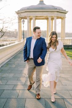 a man and woman are walking down the sidewalk in front of an old gazebo