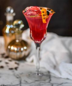 a red drink with orange garnish in a glass on a white table cloth