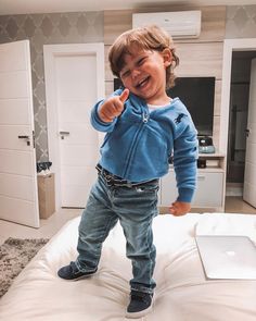 a little boy standing on top of a bed pointing at the camera with his finger