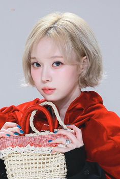 a young woman is holding a basket in her hands and looking at the camera while wearing a red coat