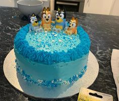 a blue frosted cake with cartoon figures on top and sprinkles around the edges