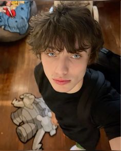 a young man with blue eyes looking up at the camera while sitting on a wooden floor