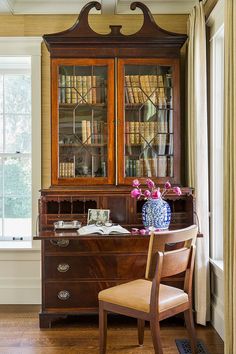 a desk with a chair, vase and bookshelf in front of a window