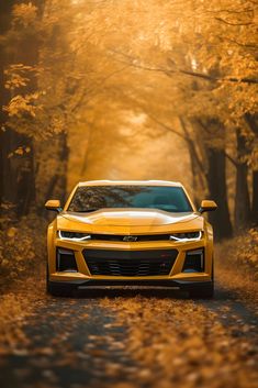 a yellow chevrolet camaro driving down a road in the woods with trees and leaves