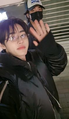 a man wearing glasses and a black jacket holds his hand up in front of him