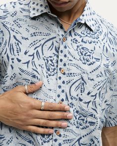 a man in a blue shirt with his hand on his chest, wearing a ring