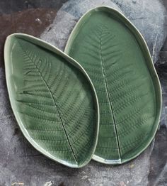 two green leaf shaped plates sitting on top of a stone slab next to each other