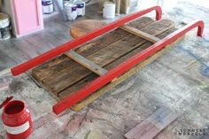 a wooden sled sitting on top of a floor next to a red bucket and paint roller