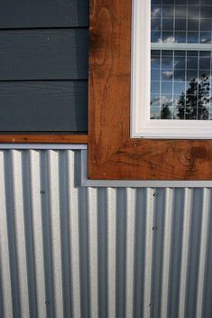 a window on the side of a building with metal siding and wood trim around it