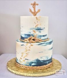 a white and blue cake with an anchor on top is sitting on a gold platter