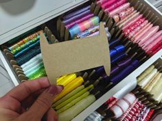 a person holding up a piece of cardboard in front of many different colored crayons