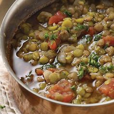 a pot filled with beans and vegetables on top of a wooden table next to a cloth