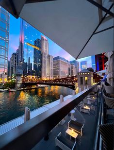 the city skyline is lit up at night as seen from an outdoor dining area with tables and chairs