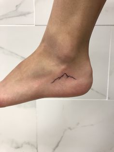 a foot with a small mountain tattoo on it's left side, in front of a tiled wall